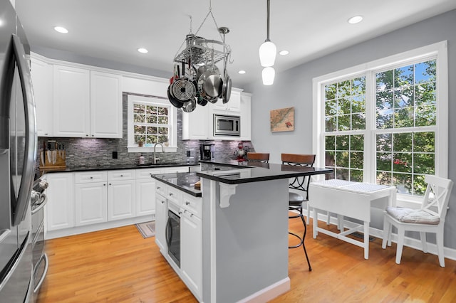 kitchen featuring decorative backsplash, a kitchen bar, a sink, light wood finished floors, and stainless steel appliances