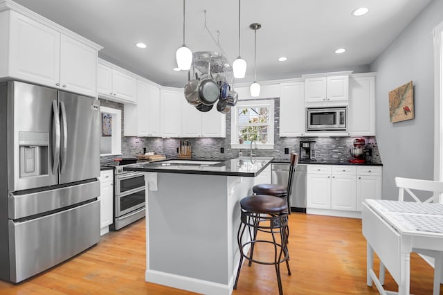 kitchen with white cabinets, dark countertops, a breakfast bar area, stainless steel appliances, and tasteful backsplash