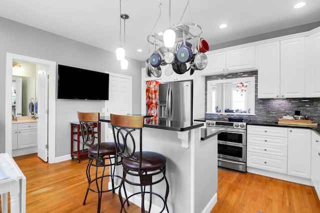 kitchen with white cabinets, dark countertops, appliances with stainless steel finishes, a breakfast bar, and light wood-type flooring