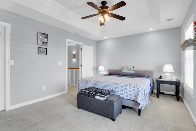 bedroom with a tray ceiling, light colored carpet, ceiling fan, and visible vents