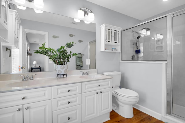 bathroom featuring wood finished floors, double vanity, a sink, and a stall shower