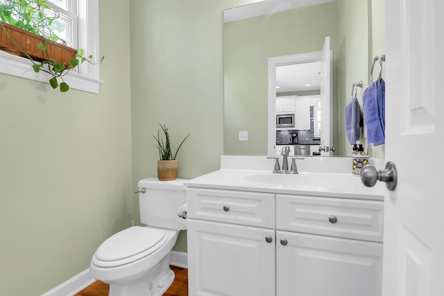bathroom featuring toilet, baseboards, wood finished floors, and vanity
