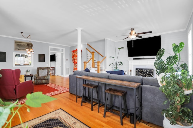 living area with a ceiling fan, a fireplace, wood finished floors, ornamental molding, and stairs