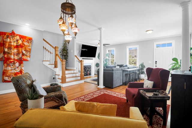 living area with a fireplace, stairs, a ceiling fan, wood finished floors, and ornate columns