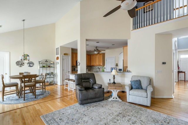 living room with baseboards, a ceiling fan, light wood-style floors, and high vaulted ceiling