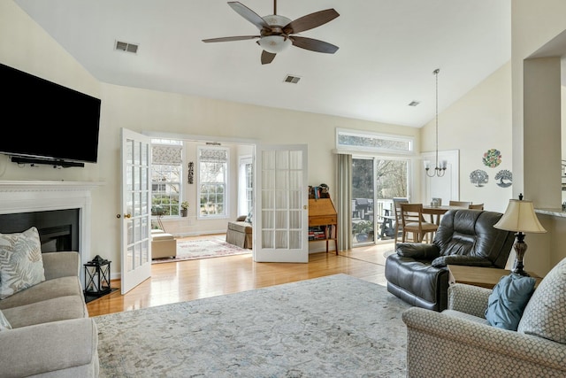 living area featuring visible vents, plenty of natural light, ceiling fan with notable chandelier, and wood finished floors