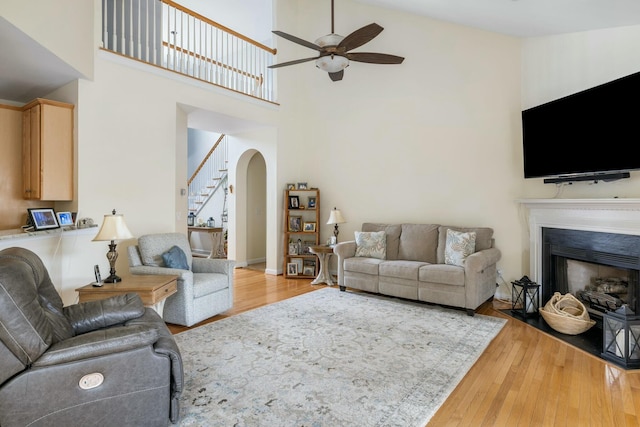 living area featuring wood-type flooring, arched walkways, ceiling fan, and stairs