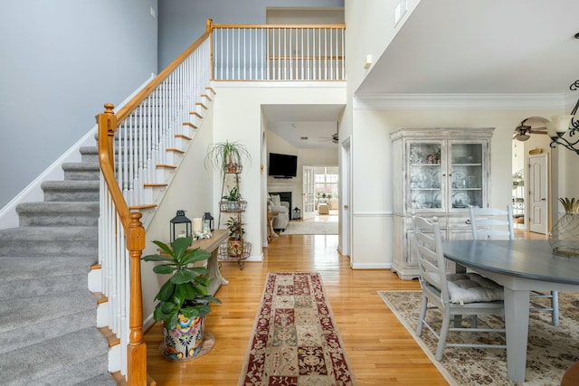 foyer entrance with stairway, wood finished floors, a high ceiling, and ornamental molding