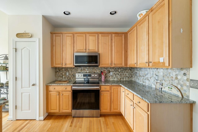 kitchen with backsplash, light brown cabinets, dark stone counters, light wood-type flooring, and appliances with stainless steel finishes