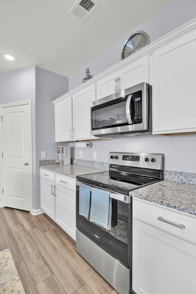 kitchen with visible vents, light wood-style flooring, light stone counters, stainless steel appliances, and white cabinetry