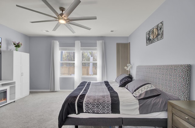 carpeted bedroom featuring baseboards, a glass covered fireplace, visible vents, and a ceiling fan