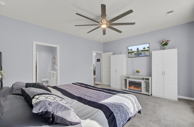 bedroom featuring light colored carpet, visible vents, ceiling fan, ensuite bath, and a warm lit fireplace