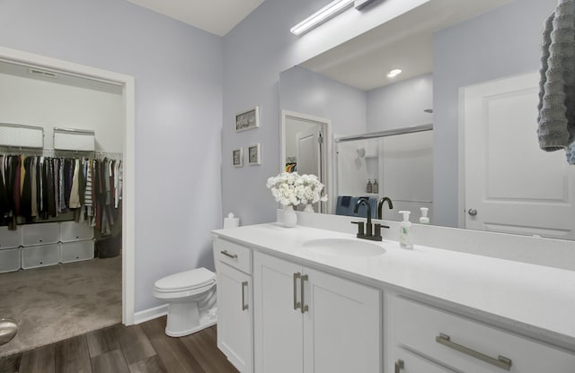 bathroom with a stall shower, toilet, wood finished floors, a walk in closet, and vanity