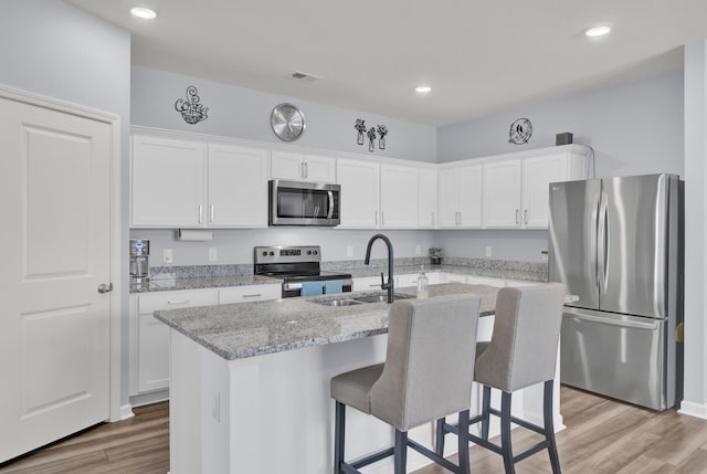 kitchen with light wood finished floors, white cabinets, an island with sink, stainless steel appliances, and a sink