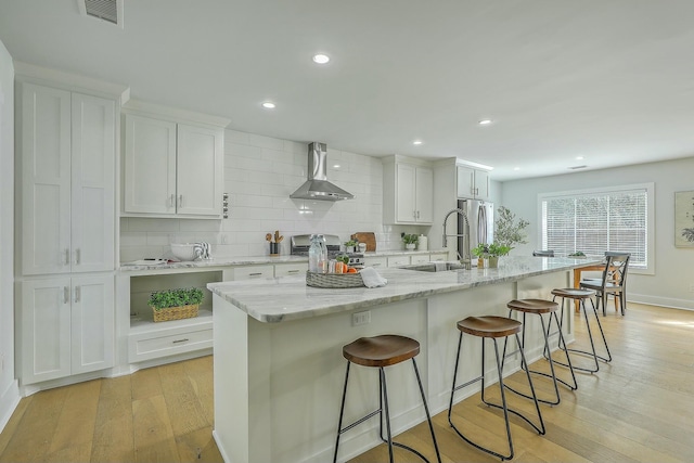 kitchen featuring a large island, stainless steel appliances, white cabinets, wall chimney range hood, and backsplash