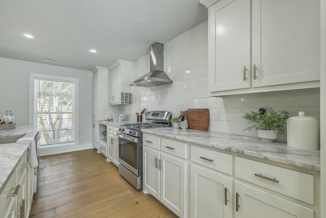 kitchen with light stone countertops, extractor fan, stainless steel gas range, backsplash, and white cabinetry