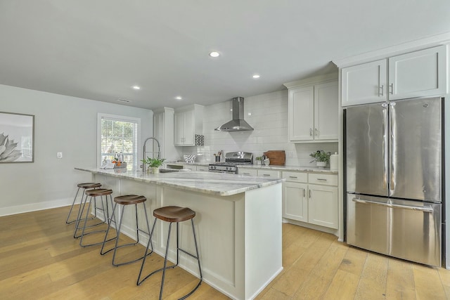 kitchen with an island with sink, appliances with stainless steel finishes, white cabinetry, and ventilation hood