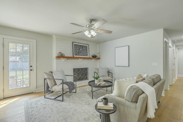 living room with a brick fireplace, ceiling fan, and light hardwood / wood-style flooring