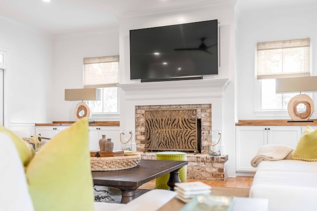 living room with crown molding, light hardwood / wood-style flooring, a wealth of natural light, and a brick fireplace