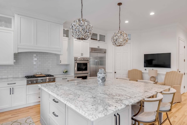 kitchen featuring light wood-type flooring, light stone counters, stainless steel appliances, white cabinets, and a center island