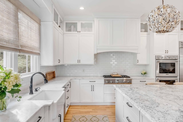 kitchen with backsplash, light hardwood / wood-style flooring, appliances with stainless steel finishes, decorative light fixtures, and white cabinetry