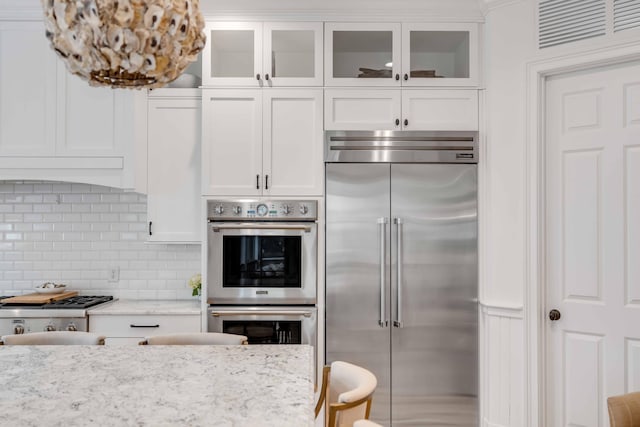 kitchen featuring white cabinets, backsplash, light stone countertops, and stainless steel appliances