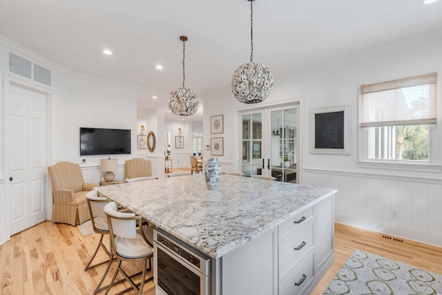 kitchen featuring hanging light fixtures, light hardwood / wood-style flooring, a kitchen island, light stone counters, and a breakfast bar area