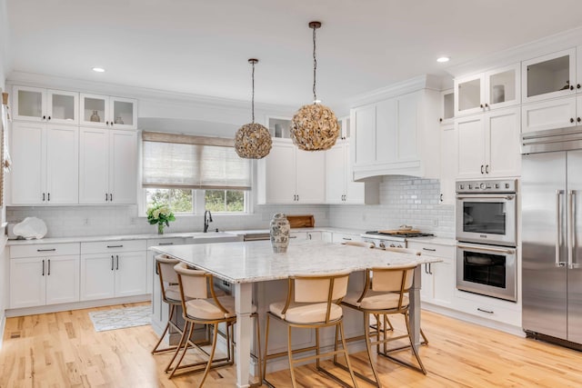 kitchen featuring white cabinetry, a center island, stainless steel appliances, light hardwood / wood-style floors, and decorative light fixtures