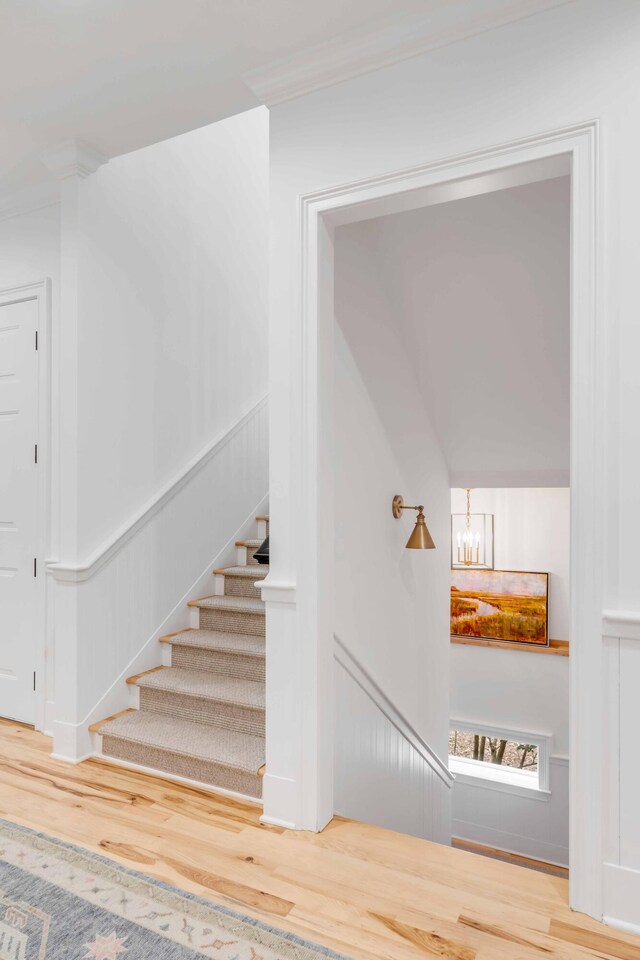 stairway featuring wood-type flooring, an inviting chandelier, and crown molding