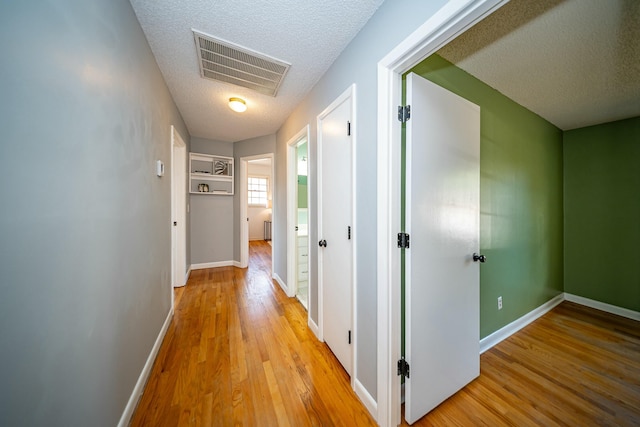 corridor with light hardwood / wood-style flooring and a textured ceiling