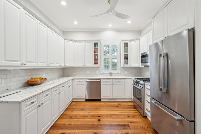 kitchen with ornamental molding, appliances with stainless steel finishes, light stone countertops, and white cabinets