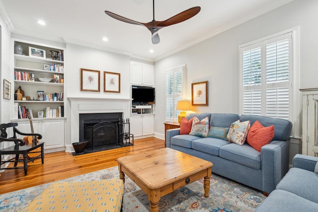 living room with crown molding, ceiling fan, built in shelves, and light hardwood / wood-style floors