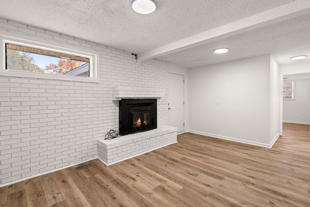 unfurnished living room featuring wood-type flooring, a textured ceiling, a brick fireplace, and brick wall