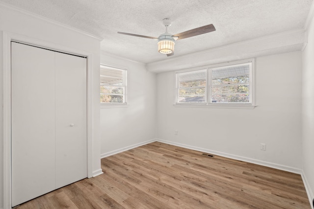 unfurnished bedroom with ceiling fan, light wood-type flooring, a textured ceiling, a closet, and ornamental molding