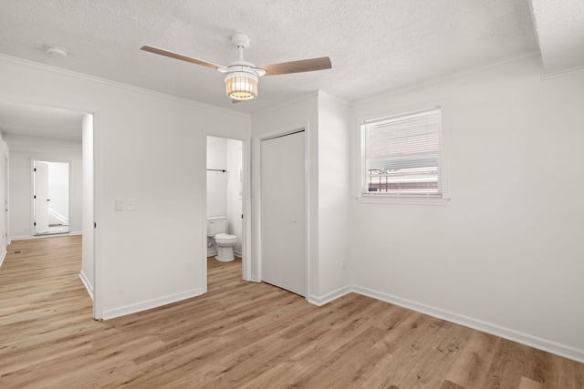 unfurnished bedroom featuring crown molding, ensuite bath, ceiling fan, light wood-type flooring, and a closet