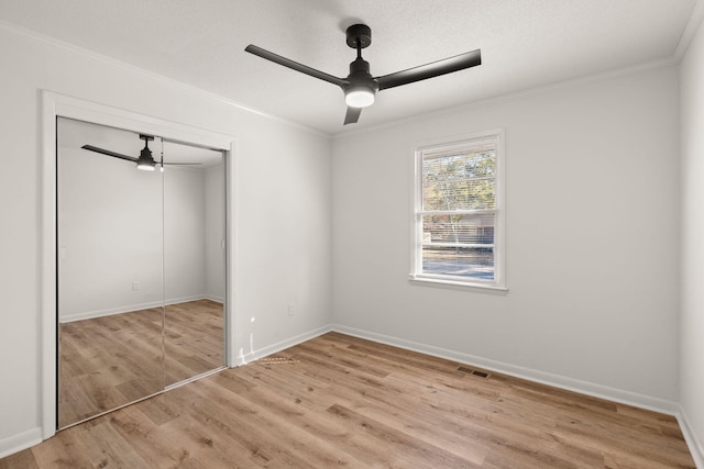 unfurnished bedroom featuring light wood-type flooring, a textured ceiling, ceiling fan, crown molding, and a closet