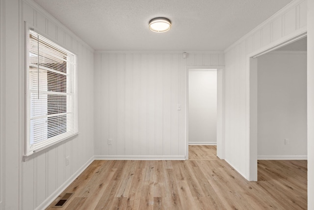 empty room featuring a textured ceiling, light hardwood / wood-style floors, and crown molding