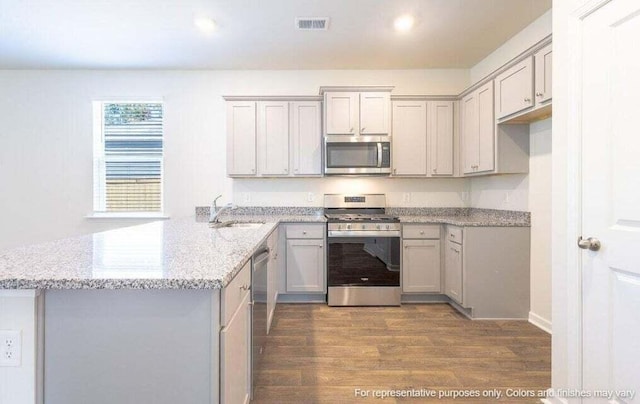 kitchen featuring light stone counters, dark wood-style floors, visible vents, a peninsula, and stainless steel appliances