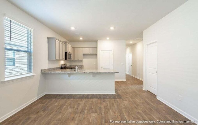 kitchen with dark wood-style floors, appliances with stainless steel finishes, a peninsula, and gray cabinetry