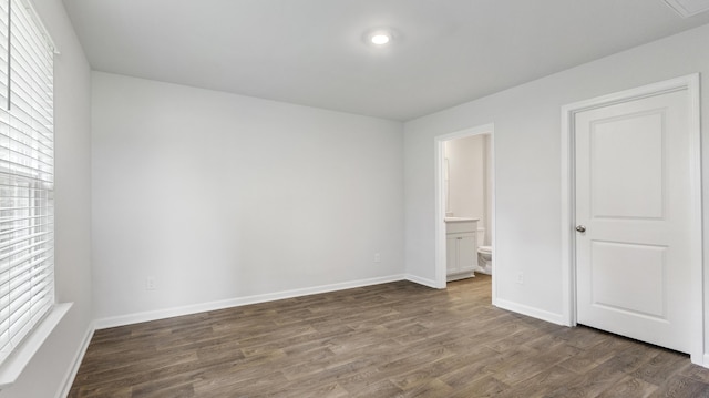 unfurnished bedroom featuring dark wood finished floors, connected bathroom, and baseboards