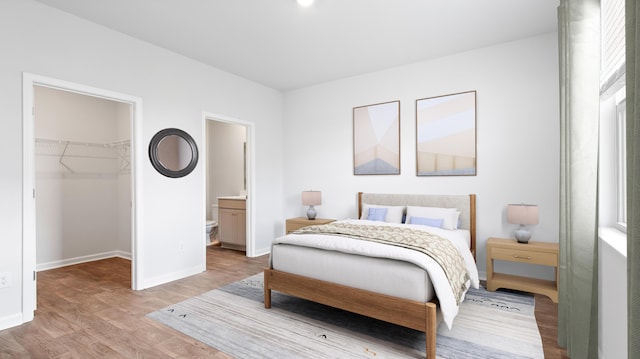 bedroom featuring light wood-style flooring, connected bathroom, a closet, baseboards, and a spacious closet