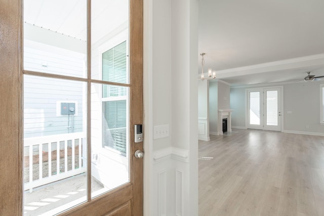 doorway with crown molding, light hardwood / wood-style flooring, and ceiling fan with notable chandelier