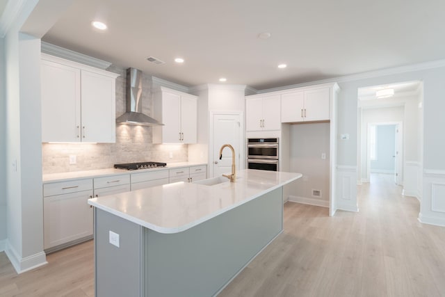 kitchen with white cabinets, wall chimney range hood, sink, and a kitchen island with sink