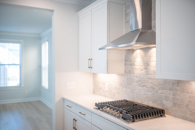 kitchen with wall chimney exhaust hood, decorative backsplash, white cabinetry, and light hardwood / wood-style flooring