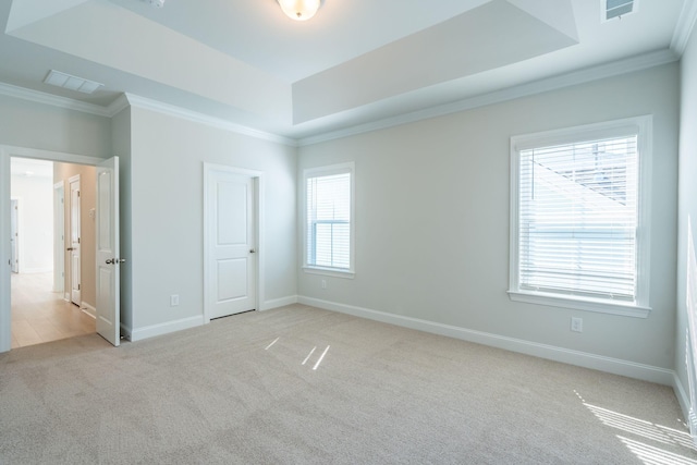 unfurnished bedroom with a tray ceiling, multiple windows, light colored carpet, and ornamental molding