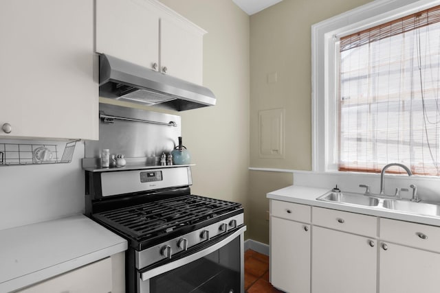 kitchen with dark tile patterned floors, sink, stainless steel gas range oven, and white cabinetry