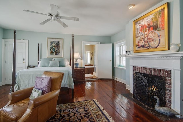 bedroom with a brick fireplace, connected bathroom, dark hardwood / wood-style flooring, and ceiling fan