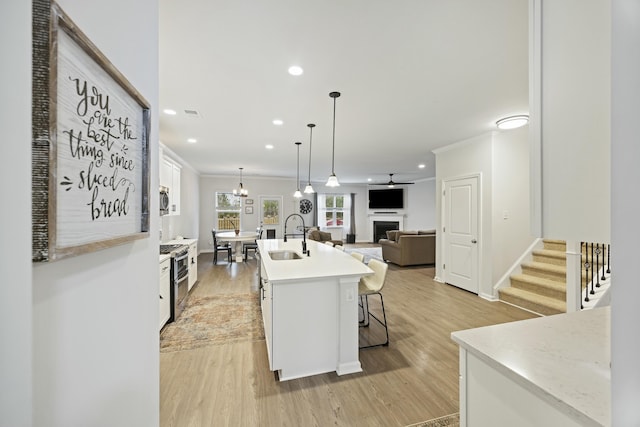 kitchen with white cabinetry, sink, a kitchen breakfast bar, hanging light fixtures, and a center island with sink