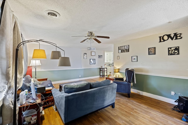 living room featuring ceiling fan, wood-type flooring, and a textured ceiling