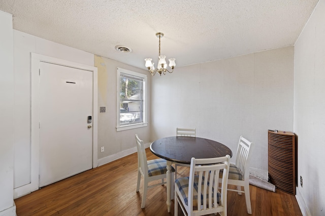 dining space with dark hardwood / wood-style floors, a textured ceiling, and an inviting chandelier